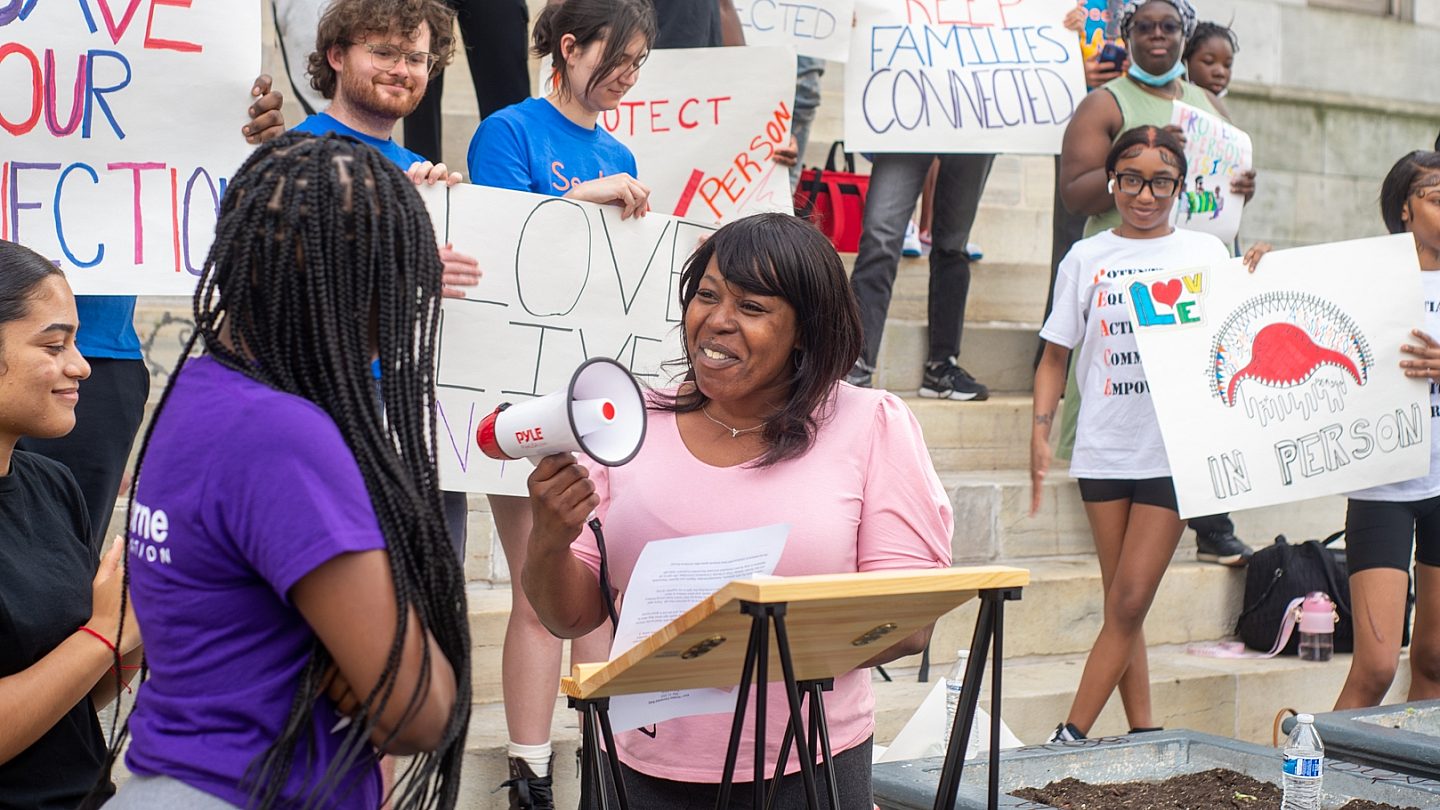 Osborne Speakers Bureau member Shameeka France smiles while standing at the podium facing a YAC member. Both are surrounded by YAC members.