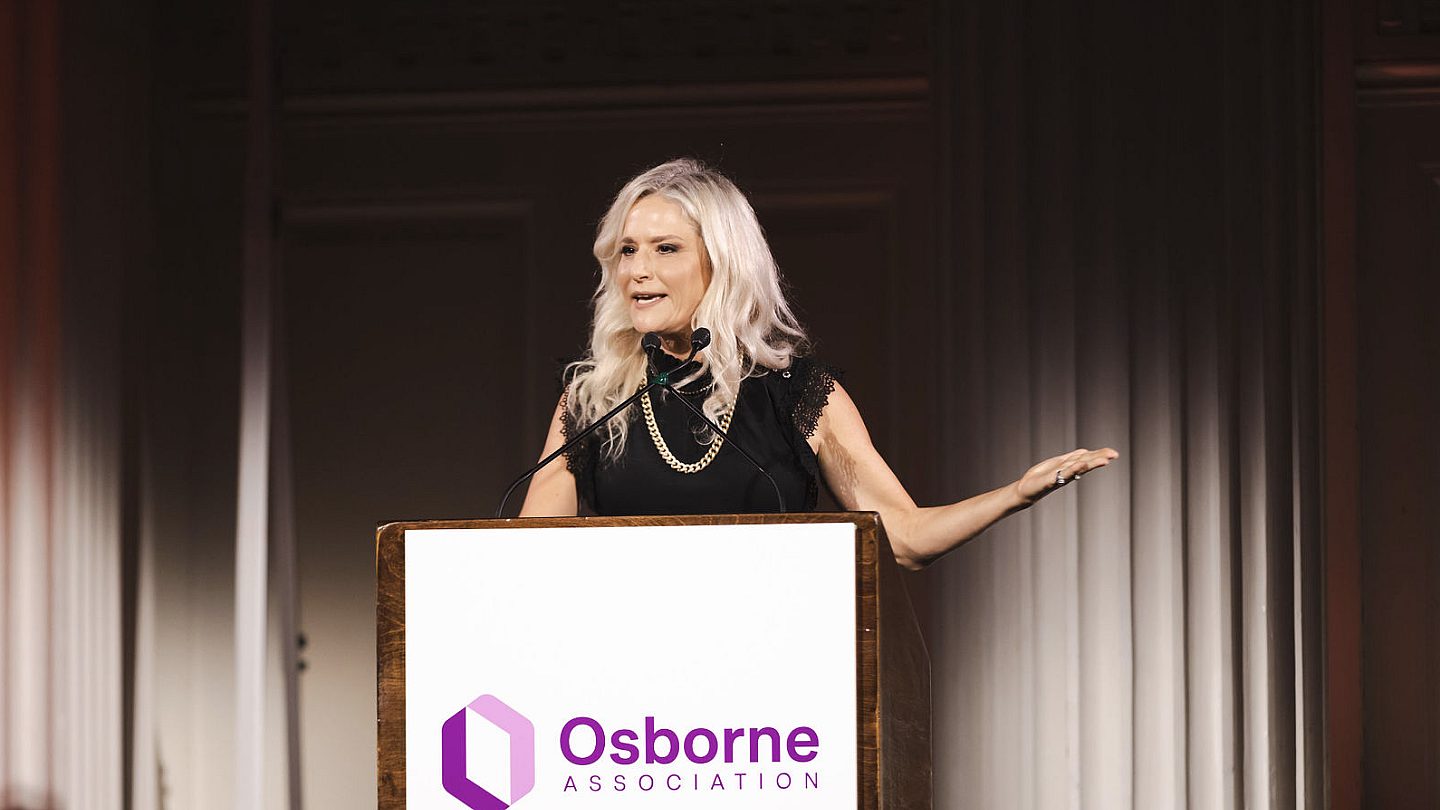 Cat Greenleaf stands on stage with her right hand outstretched.