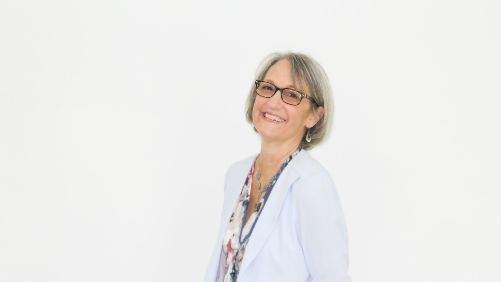 Patricia Ritchings looks at the camera with a slight smile turned in a 3/4 position with her hands gathered behind her.