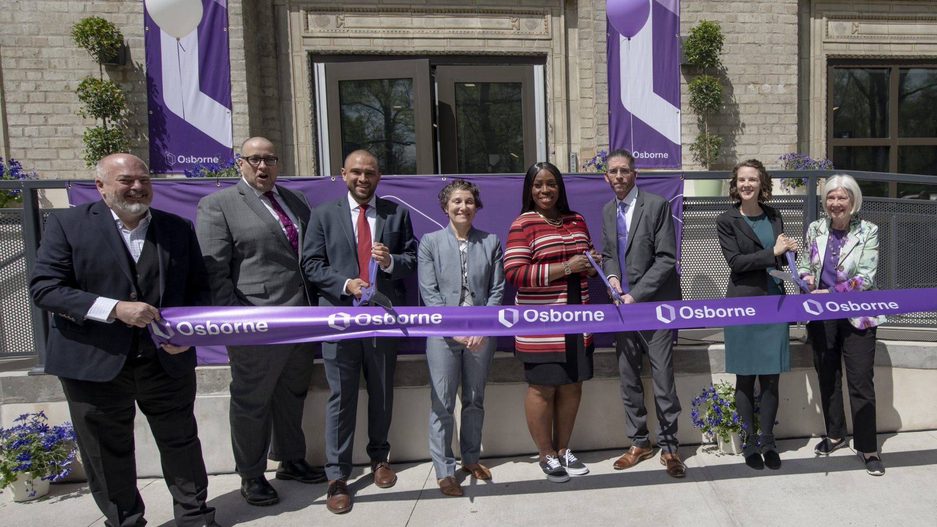 Osborne staff and partners stand together while holding three pairs of scissors to cut a giant purple ribbon.
