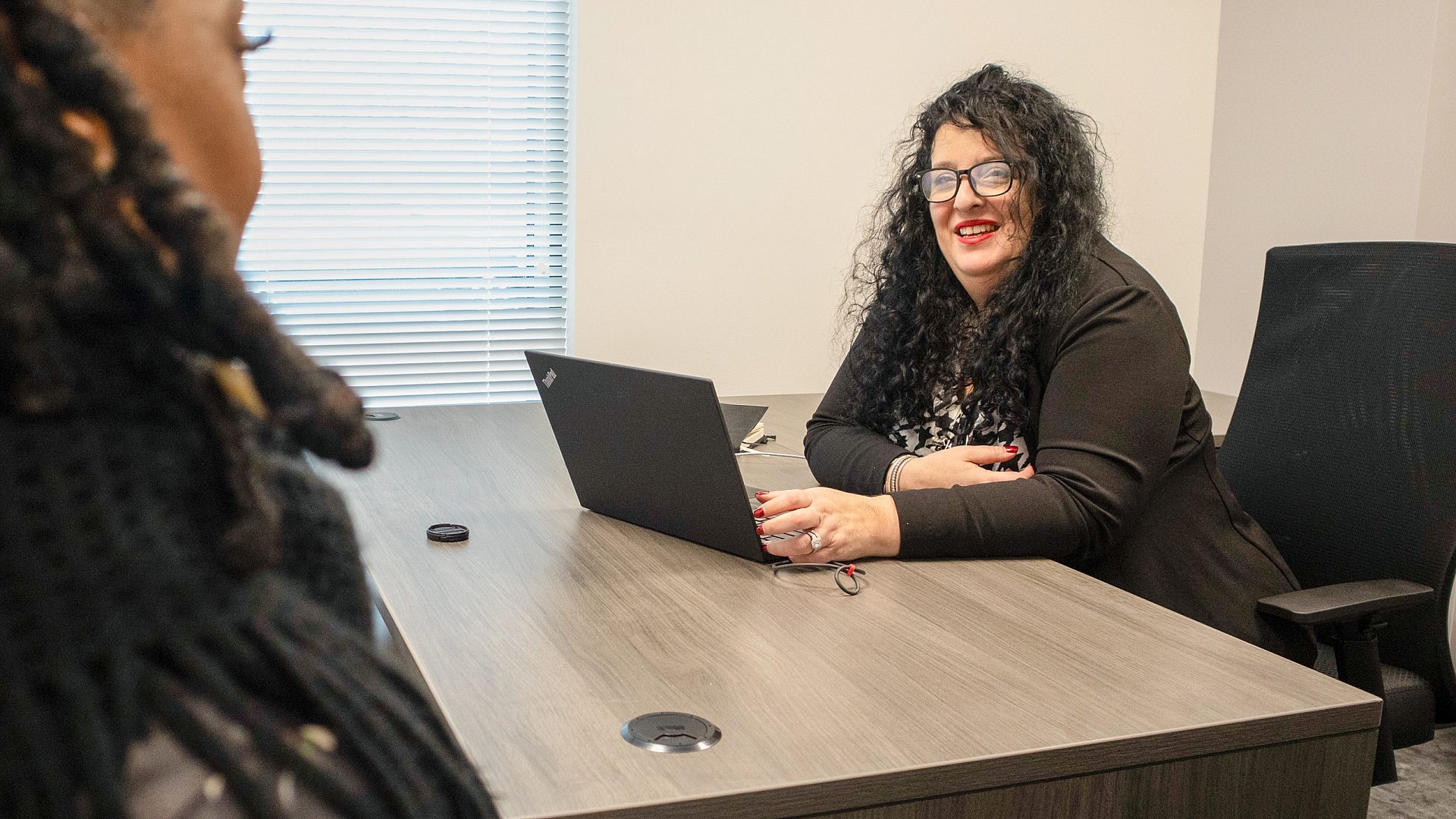 Marcus Garvey Program Director Christina Green smiling and sitting at her computer while in her office with a participant.