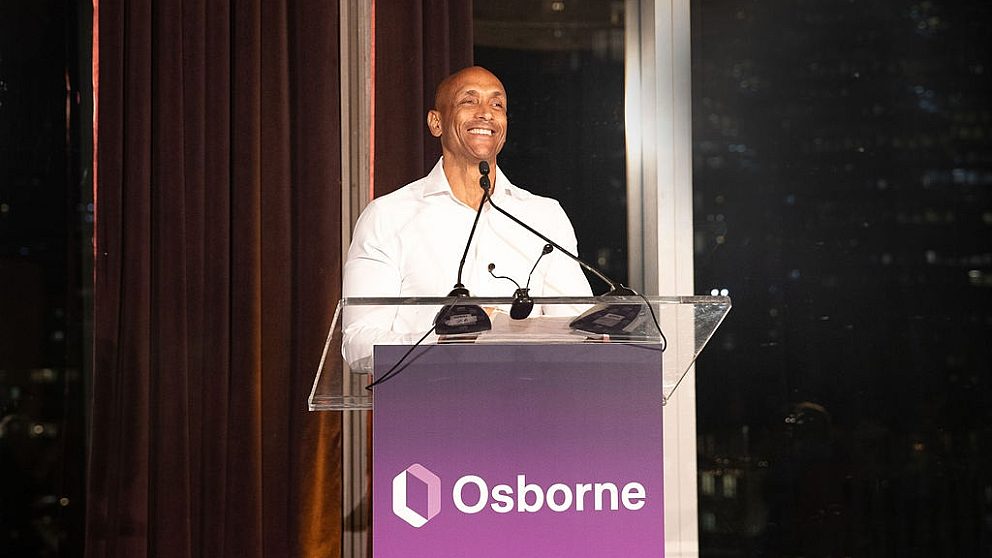 Mat stands at the podium in a white collar button up shirt smiling at the crowd.